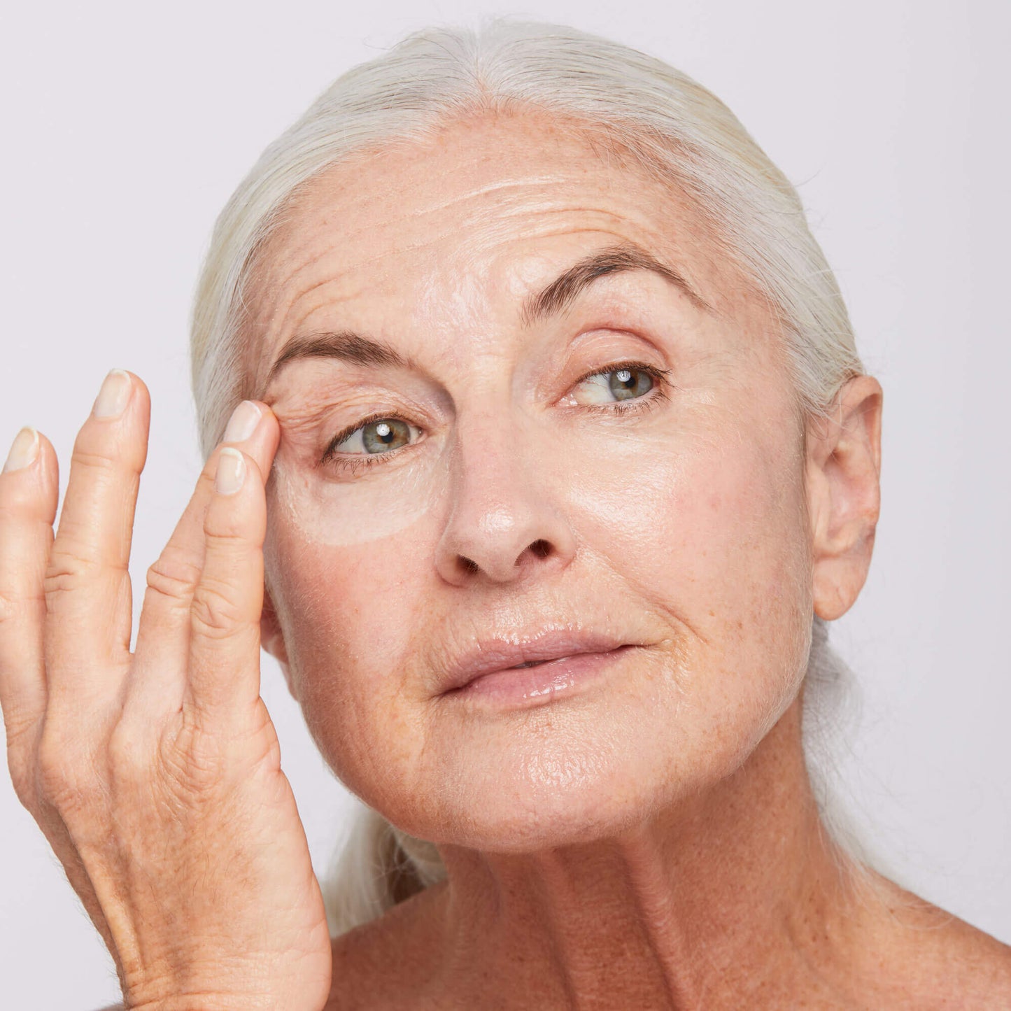 Woman applying age reversal eye complex to under eye